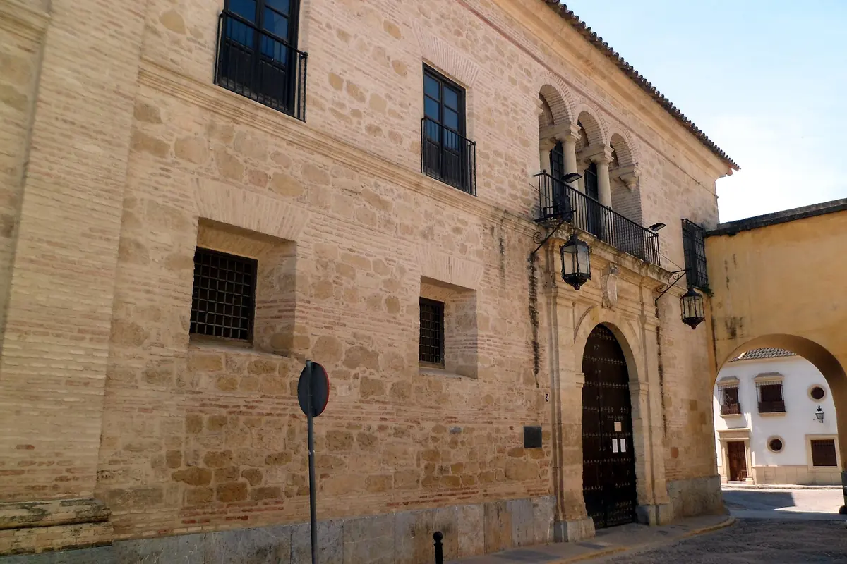 The sandstone street front of the Caballerizas Reales, with an arched door, barred windows and a balcony with lanterns.