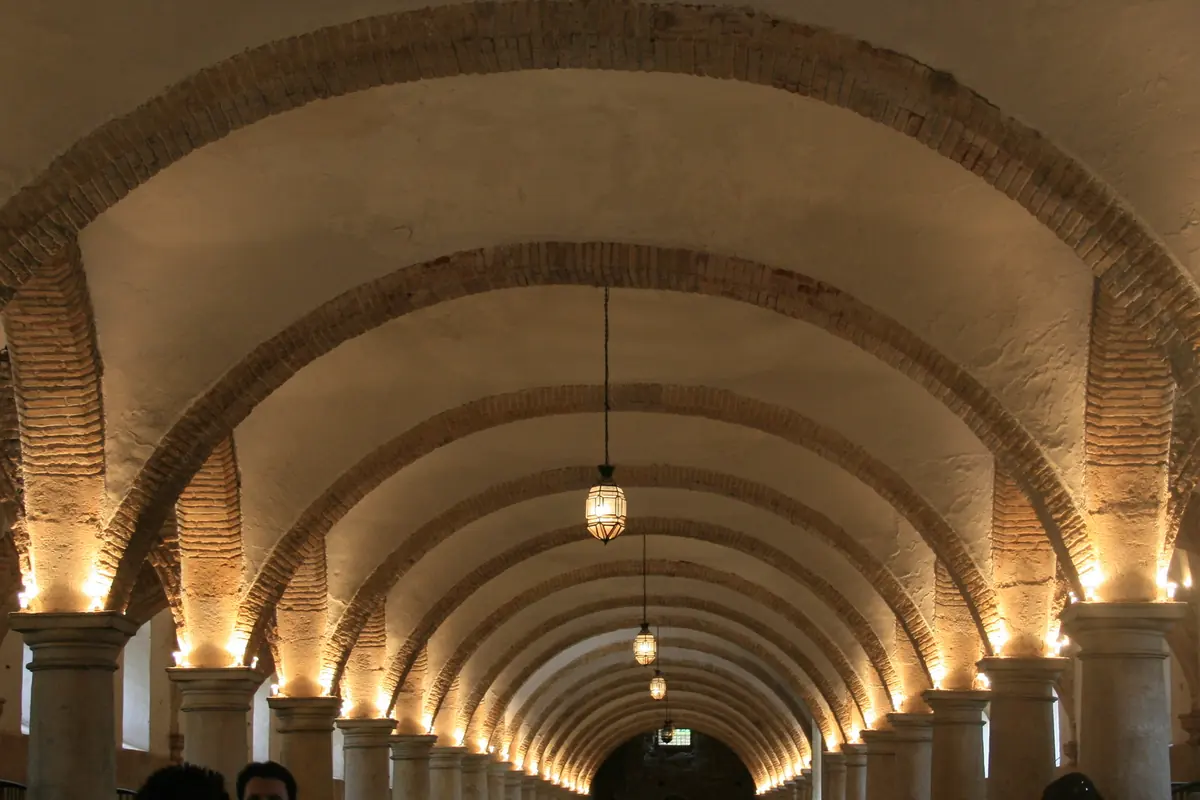 A long stone and brick stable hall lit from below, with rows of arches and groin vaults.